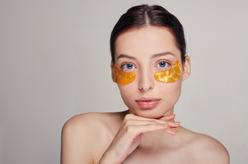 Young ptitty girl applying golden collagen patches under her eyes. Remove wrinkles and dark circles.