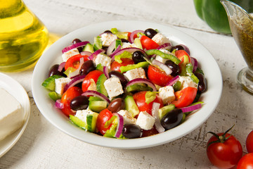 Traditional Greek salad in a round white salad bowl on an white wooden table. Selected focus.
