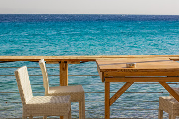 patio cafe wooden table and white chairs outdoor comfortable space for eating on sea shoreline waterfront district background, empty copy space for your text or inscription 