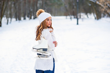 Young girl in warm clothes with ice skates on her shoulder, on a background of winter city park,...