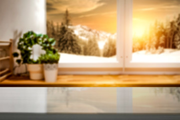Wooden table top with a blurred kitchen background and snowy winter view outside the window. Empty...