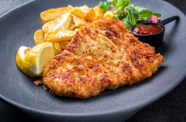 Deed fried Wiener schnitzel from veal topside with French fries and lettuce as closeup on a modern design plate