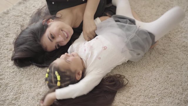 Portrait of a smiling Middle Eastern young woman playing with her daughter at the soft carpet. Happy mother spending cozy evening with her adorable child.
