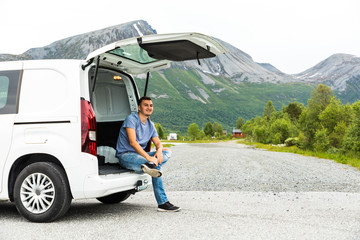 Young man sits in the car trunk on mountains view