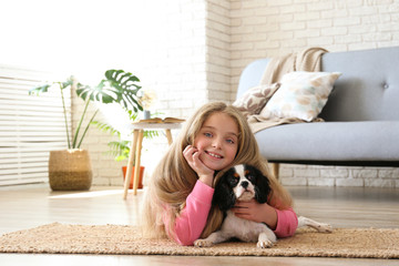 Portrait of little girl with long blonde straight hair playing with black and white Cavalier King...