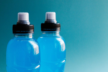 Two bottles of blue clear liquid, sports energy drink on a blue background. Selective focus