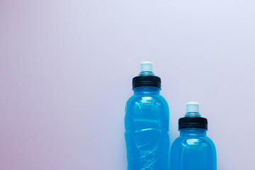 Two bottles of blue clear liquid, sports energy drink on a pink background. Selective focus