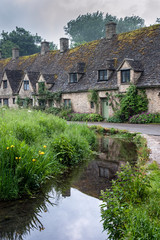 BIBURY, COTSWOLDS, UK - MAY 28, 2018: Traditional cotswold stone cottages built of distinctive yellow limestone in the world famous Arlington Row, Bibury, Gloucestershire, England   