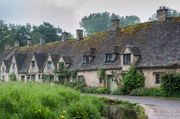 BIBURY, COTSWOLDS, UK - MAY 28, 2018: Traditional cotswold stone cottages built of distinctive yellow limestone in the world famous Arlington Row, Bibury, Gloucestershire, England   