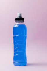 Bottle with blue clear liquid, sports energy drink on pink background. Selective focus