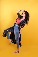 stylish girl in jeans and a lightweight full-length summer coat isolated on a yellow background
