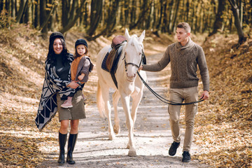 Young family is learning to ride a beautiful white horse in the autumn forest. Riding lesson - Powered by Adobe