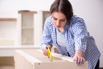 Young beautiful woman assembling furniture at home