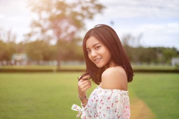 A beautiful Japanese woman wearing a white dress, walking happily in the green lawn. In the light of the sun