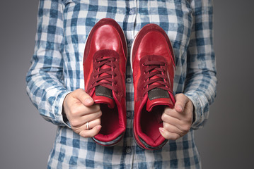 Woman with a pair of new red sport shoes in hands on gray background.