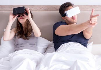 Wife and husband with virtual reality goggles in the bed