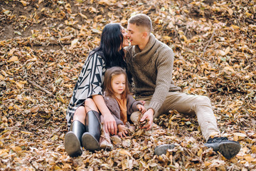 young family in the autumn forest sits on the ground covered with yellow leaves