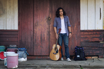 Long haired man that looks cool He is a traveler or nomadic musician who is backpacking and guitars, walking near train track in rural.