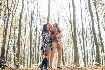 Beautiful young family walking in the autumn forest. Family walking in an autumn park with fallen fall leaves. Warm autumn