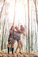 Fototapeta premium Beautiful young family walking in the autumn forest. Family walking in an autumn park with fallen fall leaves. Warm autumn