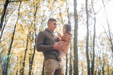 Fototapeta premium Family autumn weekend. Young father and his little daughter together in autumn park outdoors. Beautiful baby with leaves on top of dad.