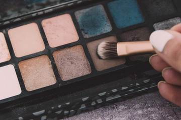 make-up brush tapping on eyeshadow with natural nude tone among other colors in a palette