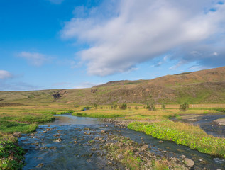 Fototapeta na wymiar Blue river stream, lush green grass meadow and hills at Reykjadalur hot springs area, South Iceland near Hveragerdi city. Summer sunny morning, blue sky.