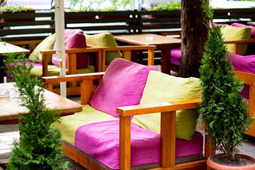 soft chairs with textile pillows of green and pink color at the wooden table of the summer street cafe.