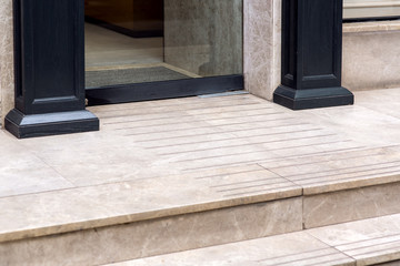 a threshold with a step from a marble tile an entrance to shop with a glass door and wooden columns...