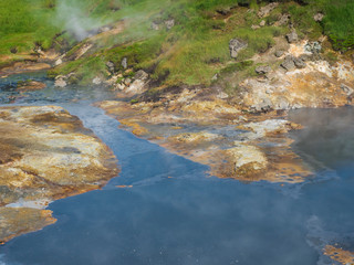 Hot geothermal blue mud pool at Reykjadalur valley with lush green grass meadowa nd steam. South...