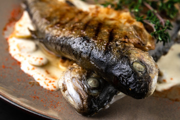 fried rainbow trout fish with lemon sauce and thyme on black marble table as background. macro view