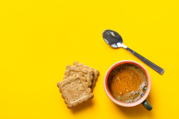 Cup of freshly brewed coffee with crema home baked bran cookies spoon on bright yellow background. Breakfast morning energy concept flat lay with copy space