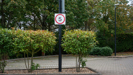 5 MPH speed sign in a tree lined carpark
