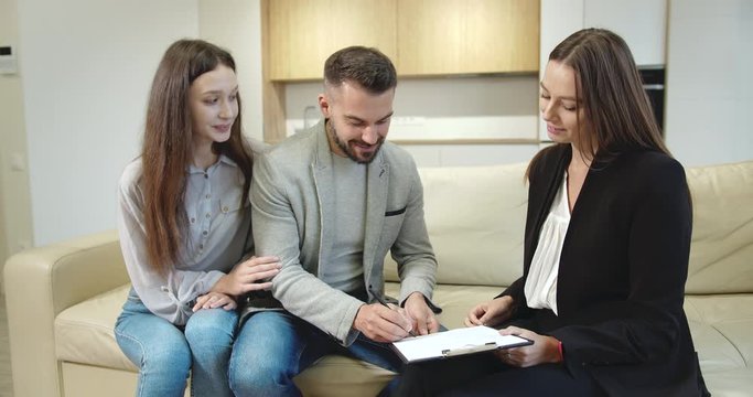 Young couple concluding deal with real estate manager, signing documents and receiving keys, moving to new home