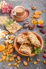 Homemade granola from oat flakes, dates, dried apricots, raisins, nuts with a cup of coffee on a black concrete background. Side view.