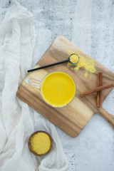 Top view of golden milk with cinnamon, styled on wooden board with loose turmeric, flat lay