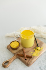 Fototapeta premium Golden milk with cinnamon, styled on wooden board with loose turmeric, alternative medicine drink, natural healing
