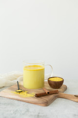 Golden milk with cinnamon, styled on wooden board with loose turmeric, alternative medicine drink, natural healing