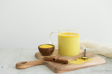 Golden milk with cinnamon, styled on wooden board with loose turmeric, alternative medicine drink, natural healing