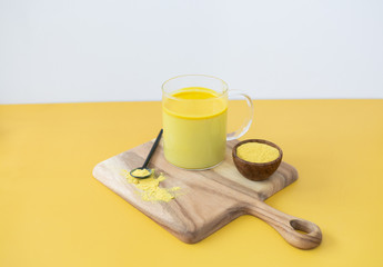 Golden milk styled on wooden board with loose turmeric, alternative medicine drink, natural healing, yellow gold background, copy space