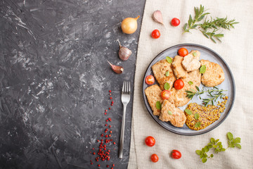 Fried pork chops with tomatoes and herbs on a gray ceramic plate on a black concrete background.  top view, copy space.
