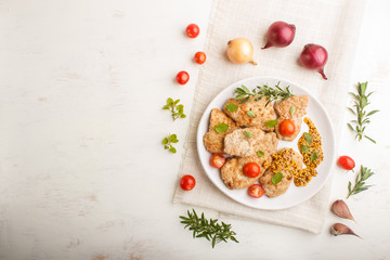 Fried pork chops with tomatoes and herbs on a white ceramic plate on a white wooden background. top view, copy space.