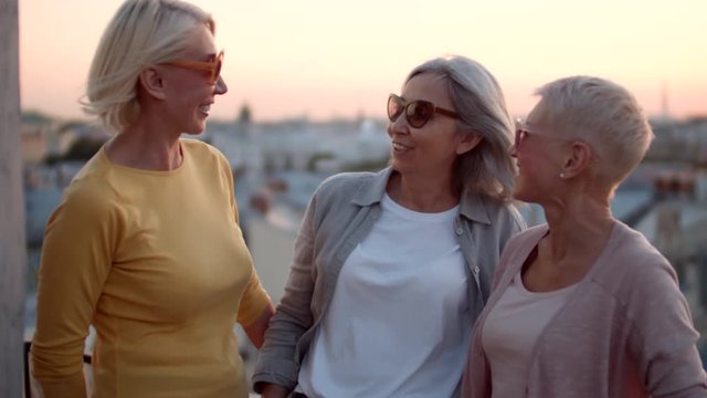 Medium shot of three middle-aged multiethnic women standing on roof and laughing while having talk