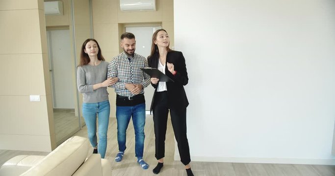 Lady real estate manager showing young man and woman apartment, family searching new home