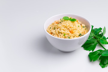 Delicious homemade vegetarian couscous with dates, raisins, parsley, tomato, lemon and olive oil in a white bowl on white background, Traditional Moroccan and Arabic Salad Tabbouleh