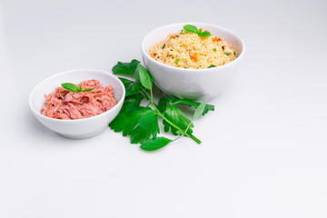 Canned tuna and delicious homemade couscous with dates, raisins, parsley, tomato, lemon and olive oil in a white bowl on white background, copy space, studio shot, soft light