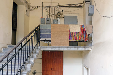 An old staircase to the upper floor. Inside the building which is located on Rustaveli street in Tbilisi, Georgia. Carpets weigh on the railing in the entrance. Many electrical panels on the wall.