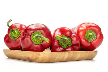 Group of four whole sweet red bell pepper on wooden square plate isolated on white background