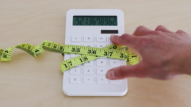 tightening up your budget, calculator wrapped up by measuring tape with big number on the screen and hand zeroing it out