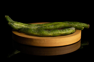 Group of three whole dry vegetable chip of green bean on bamboo coaster isolated on black glass